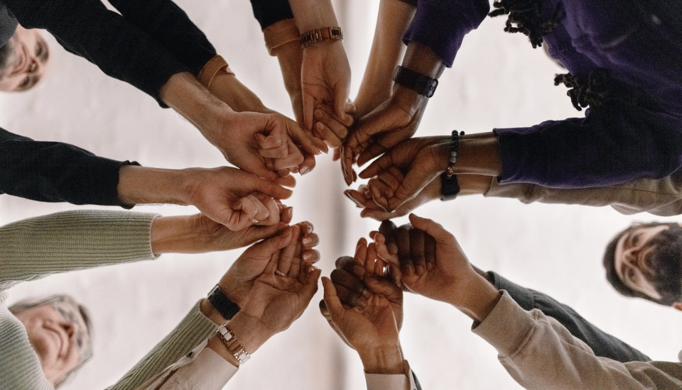 An image of people putting their hands together in the centre of a human circle in a sign of unity.